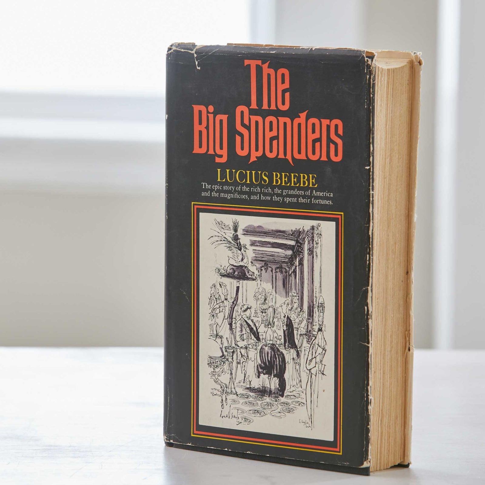 Book titled 'The Big Spenders' by Lucius Beebe on a white surface with a blurred background