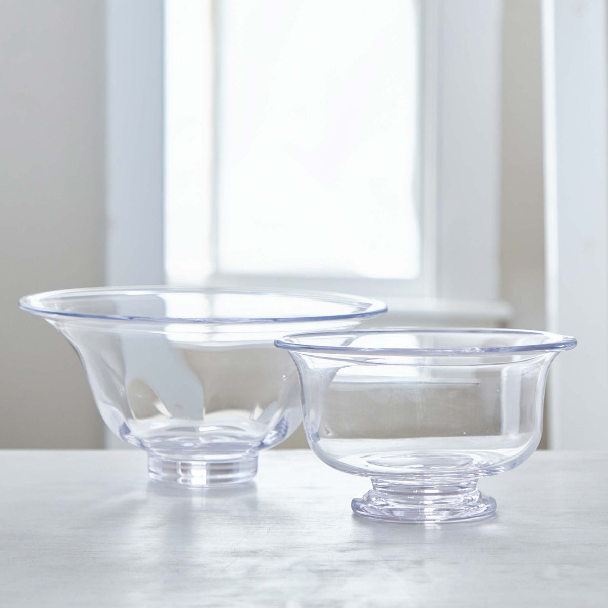 Two clear Simon Pearce glass bowls with a footed base and flared rims, one larger than the other, made of lead-free glass.